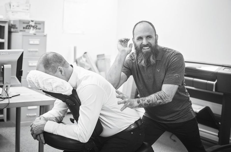 Professional massage therapist performs seated massage on man in office.