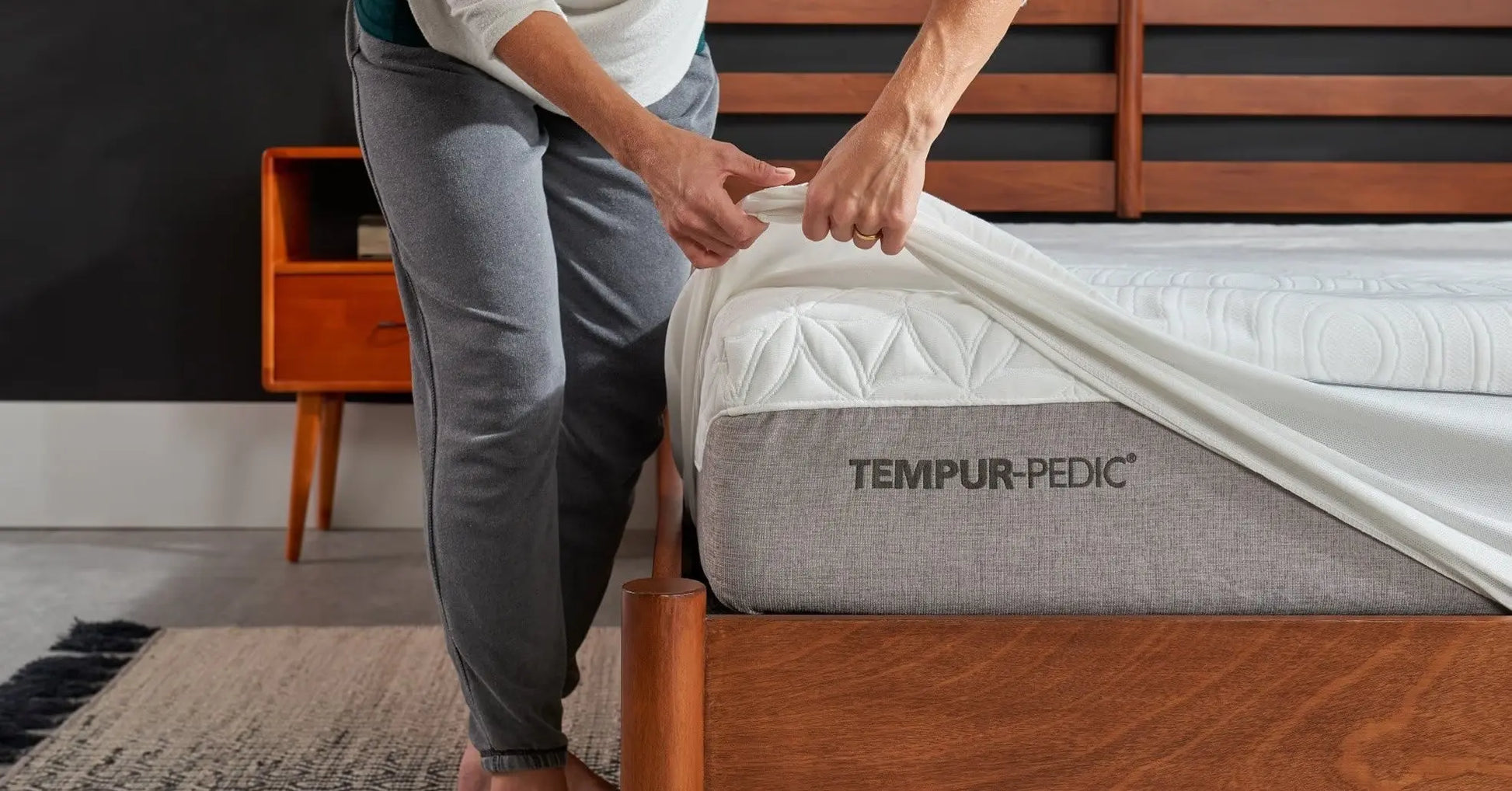 Person placing a TEMPUR-Protect mattress protector on a bed, showcasing the Tempur-Pedic bedding accessory.